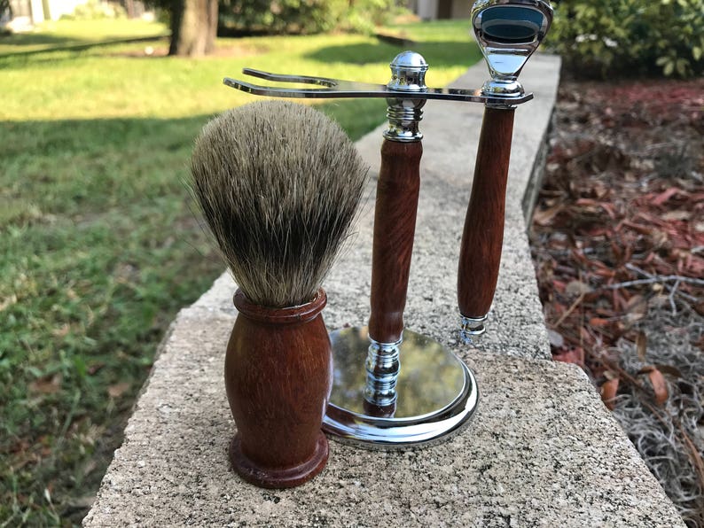 Eucalyptus shaving set with brush, stand, and razor handle sitting outside on a paver stone with grass in the background