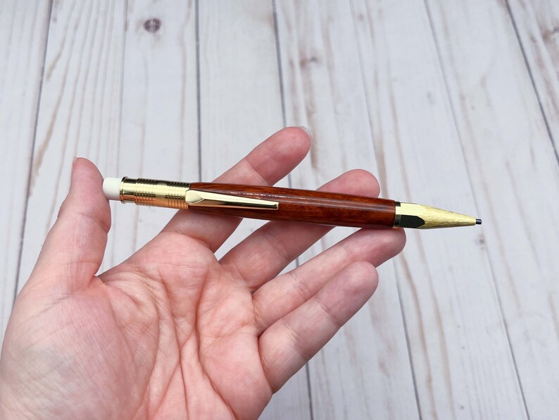 Holding the eucalyptus wood 2mm mechanical pencil under bright lights to show off the reddish brown of the wood and the gold hardware.