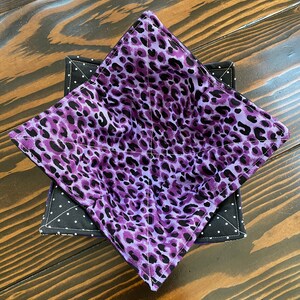 May include: A purple and black leopard print fabric bowl cozy. The cozy is folded into a bowl shape and is sitting on a wooden surface.