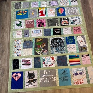 May include: A green patchwork quilt with squares of various fabrics, each featuring a different design. The squares include images of cartoon characters, band logos, and phrases like "Mama's Girl", "Big Brother", and "Stranger Things".