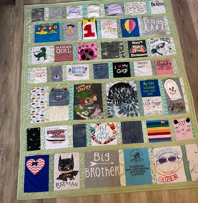 May include: A green patchwork quilt with squares of various fabrics, each featuring a different design. The squares include images of cartoon characters, band logos, and phrases like "Mama's Girl", "Big Brother", and "Stranger Things".