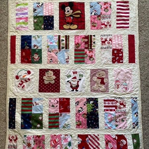 May include: A white patchwork quilt with a Christmas theme. The quilt is made up of squares of different fabrics, each with a different Christmas design. Some of the designs include snowmen, Santa Claus, reindeer, and gingerbread men. The quilt is edged with a white border.