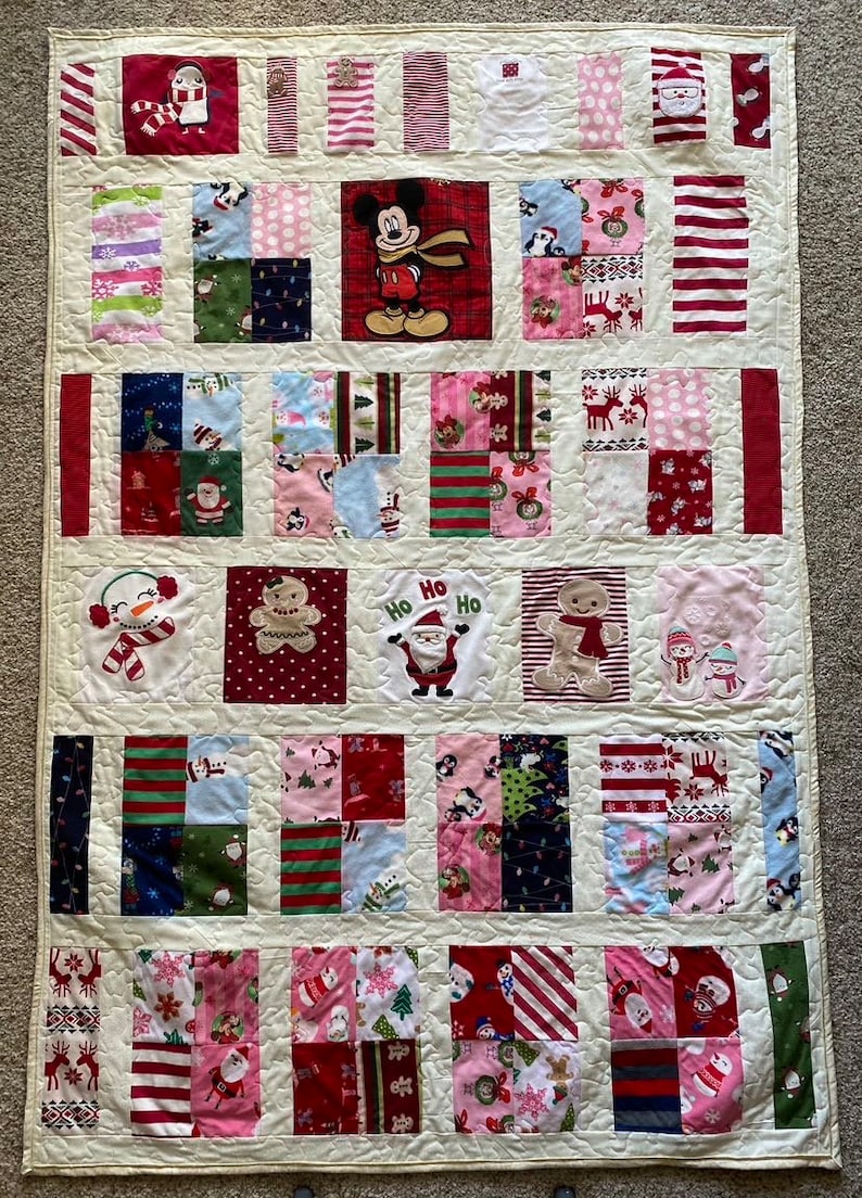 May include: A white patchwork quilt with a Christmas theme. The quilt is made up of squares of different fabrics, each with a different Christmas design. Some of the designs include snowmen, Santa Claus, reindeer, and gingerbread men. The quilt is edged with a white border.