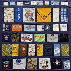 May include: A blue quilt with various patches of fabric. The patches feature different designs, including a train, a fire truck, a pumpkin, a birthday boy, and a swim school logo. The quilt is made up of a variety of colors, including blue, yellow, green, red, and orange.