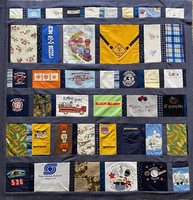 May include: A blue quilt with various patches of fabric. The patches feature different designs, including a train, a fire truck, a pumpkin, a birthday boy, and a swim school logo. The quilt is made up of a variety of colors, including blue, yellow, green, red, and orange.