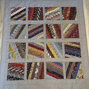 May include: A gray quilt with a patchwork design made from strips of fabric in various colors and patterns. The quilt is made from recycled neckties.