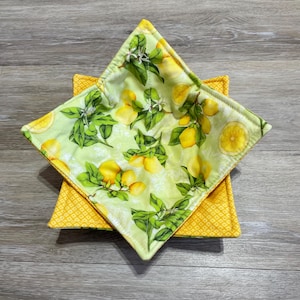 May include: A yellow and green fabric bowl with a lemon print. The bowl is made of two layers of fabric, with the top layer featuring a lemon print and the bottom layer a yellow geometric pattern.