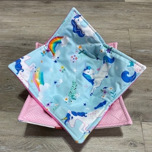 May include: A blue and pink fabric bowl with a unicorn and rainbow design. The bowl is quilted and has a pink polka dot lining.