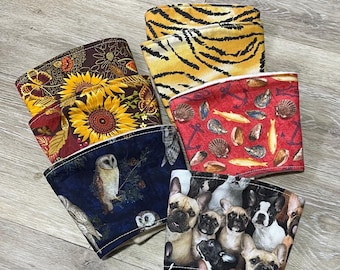 May include: A set of eight colorful fabric coffee cup sleeves. The sleeves feature various patterns, including owls, sunflowers, seashells, and French bulldogs.