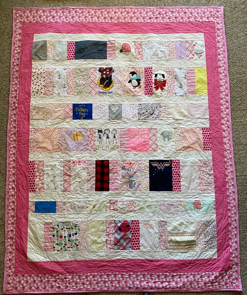 May include: A pink and white patchwork quilt with a variety of fabric squares featuring different patterns and designs, including polka dots, stripes, and animal prints. The quilt is bordered with a pink trim.