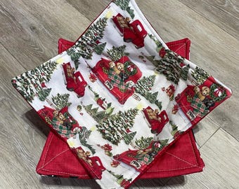 May include: Two square bowl cozies. The top cozy has a white background with a pattern of red trucks, Christmas trees, and dogs. The bottom cozy is solid red. The top cozy has a red border.
