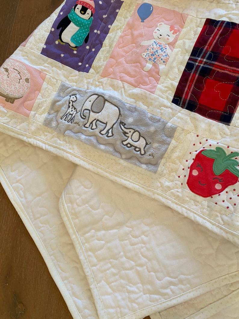 May include: A white quilted baby blanket with a variety of colorful appliques, including a penguin, a bear, elephants, and a strawberry. The blanket is made of soft, comfortable fabric and is perfect for cuddling.