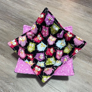 May include: A black fabric bowl with a pink and purple fabric lining. The bowl is decorated with a pattern of owls in various colors, including pink, purple, green, and blue.