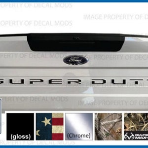 May include: A white Ford Super Duty truck tailgate with a black "SUPER DUTY" lettering decal. The image shows different decal options, including gloss black, American flag, chrome, and camouflage.