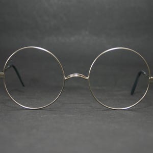 May include: Round spectacles featuring thin, polished silver-tone metal frames. The circular lenses are clear, and the temples are finished with black tips. These glasses have a simple bridge connecting the two circular rims in a symmetrical design.