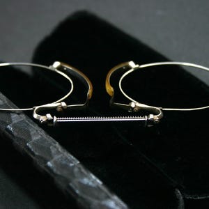 May include: Antique eyeglasses with oval lenses and a silver-colored frame. The glasses have a bridge and adjustable nose pads. They are resting on a black velvet case, suggesting a vintage or collectible item.