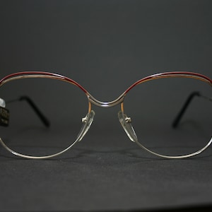 May include: Silver-rimmed glasses with a burgundy accent on the top of the frame.