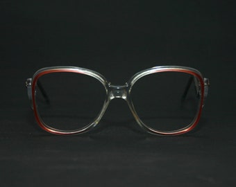 May include: Clear plastic eyeglasses with a red rim around the lenses.