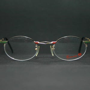 May include: Gold-rimmed oval eyeglasses with a red and green accent on the arms.