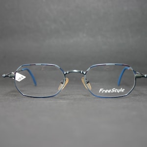 Puede incluir: Gafas de metal azul oscuro con montura de forma hexagonal. Las lentes son transparentes, con la palabra FreeStyle impresa en blanco en la lente derecha. Las varillas tienen puntas azules y las almohadillas nasales son de color ámbar.