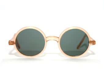 Könnte beinhalten: Runde, pfirsichfarbene Sonnenbrille mit dunkelgrauen Gläsern.