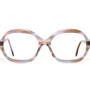 May include: Oval-shaped eyeglasses with a multi-colored frame. The frame features a blend of pink, blue, and brown hues. The lenses are clear, and the temples are a dark brown color. The glasses are set against a white background.