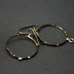 May include: Antique pince-nez eyeglasses with a tortoiseshell pattern on the rims and gold-toned metal accents. The glasses have a bridge and a small loop for a chain. The lenses are missing.