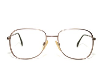 Può includere: Un paio di occhiali vintage con montatura in metallo color argento. Le lenti sono trasparenti e i naselli sono ingialliti. Le aste sono nere. Gli occhiali sono su sfondo bianco.