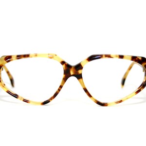 May include: Tortoiseshell-patterned spectacles with a distinctive geometric frame. The glasses display a blend of brown and yellow tones, with clear lenses. The frames have a unique shape, offering a vintage aesthetic.