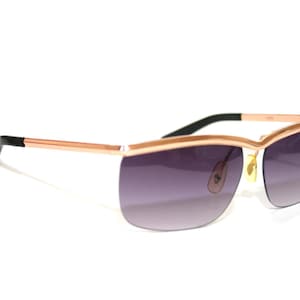May include: Rose gold sunglasses with a rimless design and gradient purple lenses. The temples are rose gold with black accents at the ear pieces. The sunglasses have a modern, sleek aesthetic.