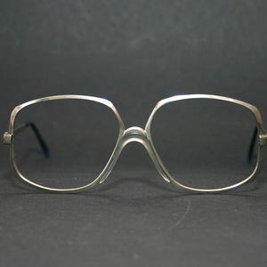 Puede incluir: Gafas de metal de color plateado con lentes cuadrados. Las gafas tienen un marco delgado y de alambre.