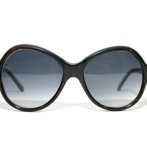 Könnte beinhalten: Schwarze ovale Sonnenbrille mit dunkelgrauen Verlaufsgläsern.