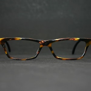 May include: Eyeglasses with a tortoiseshell pattern frame. The glasses have a rectangular shape and black temples. The frame features shades of brown, yellow, and black. The lenses are clear.