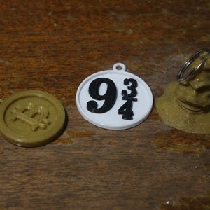 May include: Three 3D printed charms: a gold-colored Bitcoin symbol, a white circle with black numbers "9 3/4", and a gold-colored Sorting Hat.