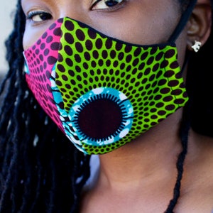 May include: A close-up of a face mask with a green, black, pink, and blue patterned design. The mask has a black elastic band.