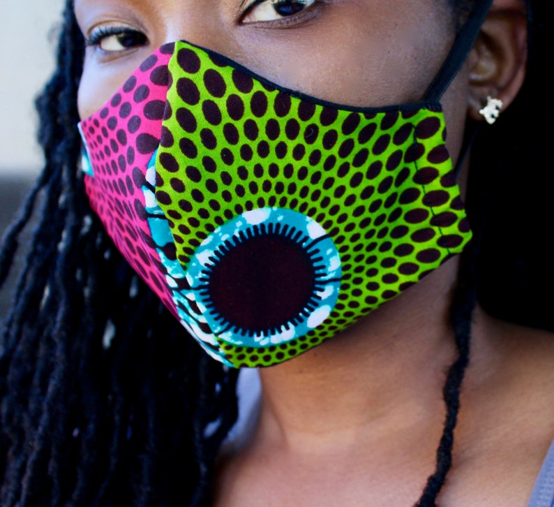 May include: A close-up of a face mask with a green, black, pink, and blue patterned design. The mask has a black elastic band.