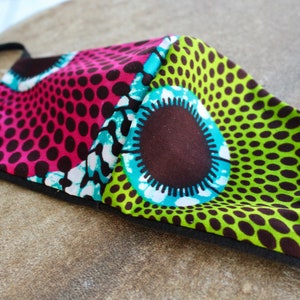 May include: A reusable face mask with a colorful geometric pattern. The mask is made of fabric and has a black elastic band. The pattern features pink, green, blue, white, and brown colors.