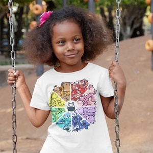 May include: A young person wearing a white t-shirt with a colorful graphic of animals arranged in a circle. The graphic includes a variety of animals, including a bear, a fish, a bird, and a cat. The person is sitting on a swing set in a playground.