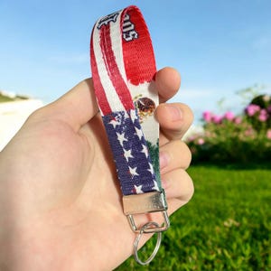 May include: A red, white, and blue key chain with a silver key ring. The key chain has the American flag on one side and the Mexican flag on the other side. The key chain is made of fabric and has a printed design.