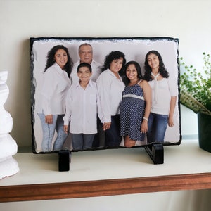 May include: A family portrait printed on a slate photo holder. The photo shows six people, including two adults, three children, and a baby. The family is dressed in casual clothing and smiling. The slate photo holder is a natural stone with a rustic look.