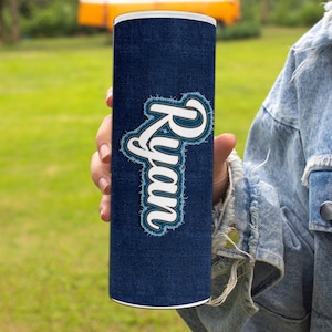 May include: A blue and white tumbler with the word "Ryan" written in a white, distressed font on a denim-like background.