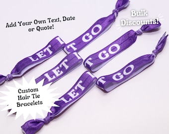May include: Purple elastic hair ties with the text "Let It Go" printed in white. The hair ties are arranged in a starburst pattern on a white background. The text "Custom Hair Tie Bracelets" is printed in a white starburst shape below the hair ties.