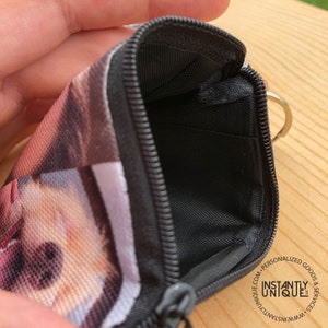 May include: A black zippered pouch with a photo printed on the front. The pouch has a black zipper and a silver key ring. The pouch is open and the inside is lined with black fabric.