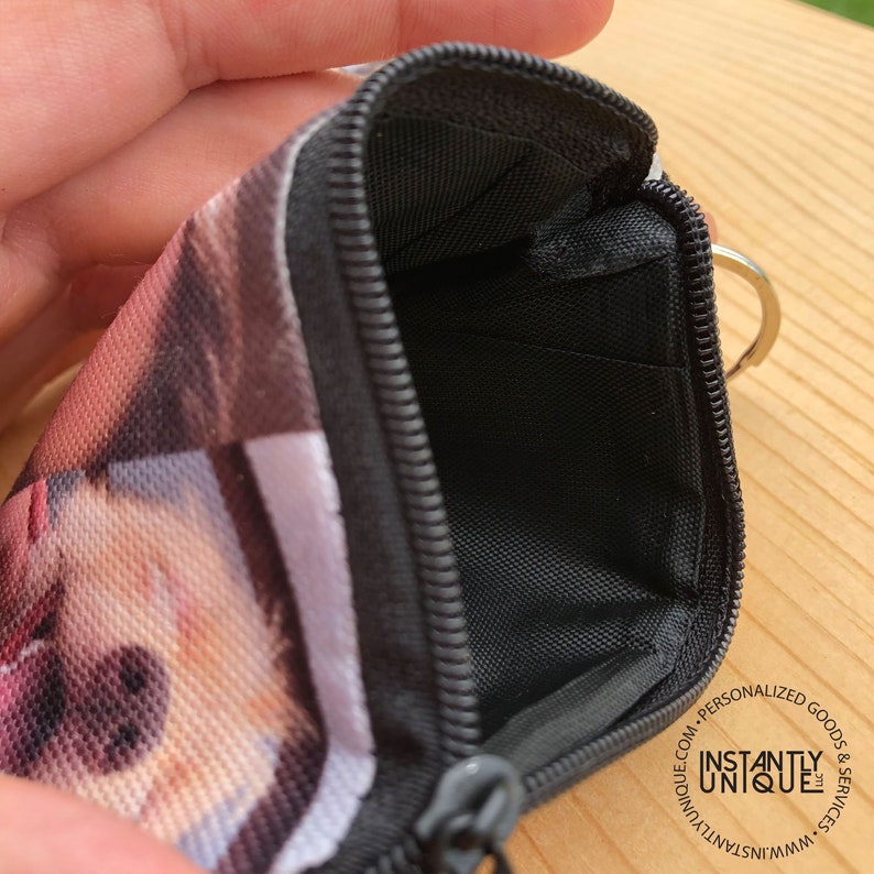 May include: A black zippered pouch with a photo printed on the front. The pouch has a black zipper and a silver key ring. The pouch is open and the inside is lined with black fabric.