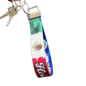May include: A green, white, and blue key chain with the Mexican flag and the word "Mexico" printed on it. The key chain has a silver metal ring.