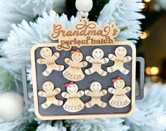 Op de afbeelding: Houten kerstornament in de vorm van een bakplaat met peperkoeken poppetjes. Het ornament leest "Grandma's perfect batch" en bevat namen als Max en Sarah. Het hangt aan een wit touwtje en houten kraal.