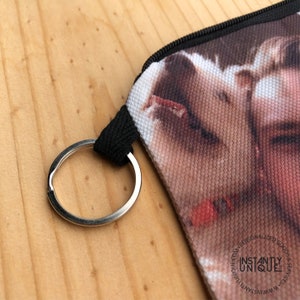 May include: A black zippered pouch with a key ring. The pouch is made of canvas and features a printed image of a dog's face. The text "INSTANTLY UNIQUE" is printed on the pouch.