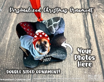 Op de afbeelding: Een gepersonaliseerde kerstversiering met een foto van een hond met een rode en witte hoed en grijze trui. De versiering heeft de tekst "Merry Christmas 2022" en "Double Sided Ornament!" met een rood lint om op te hangen.