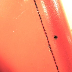 Puede incluir: Primer plano de una superficie met&aacute;lica roja con un peque&ntilde;o agujero. La superficie tiene un ligero brillo y parece estar pintada.