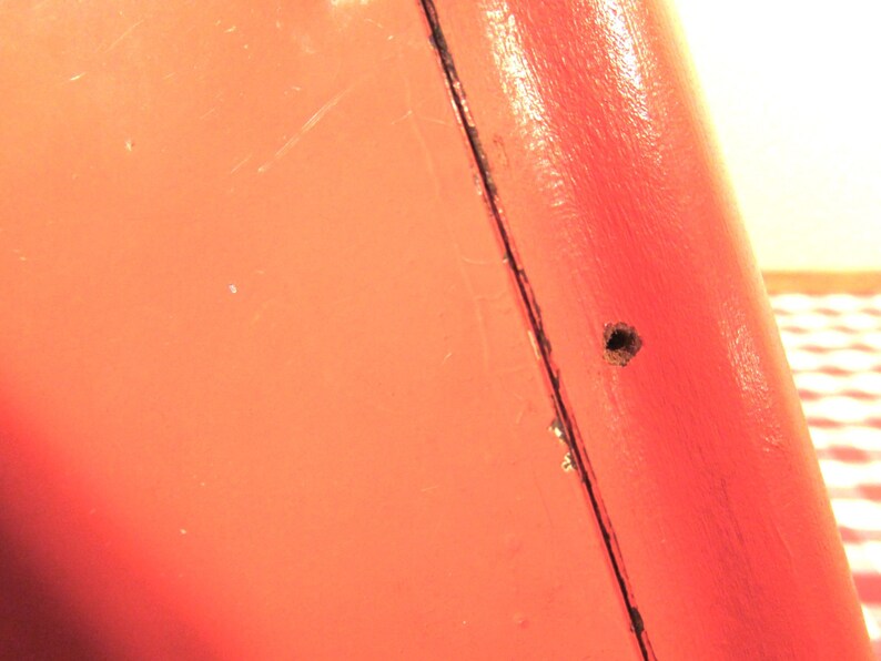Puede incluir: Primer plano de una superficie met&aacute;lica roja con un peque&ntilde;o agujero. La superficie tiene un ligero brillo y parece estar pintada.